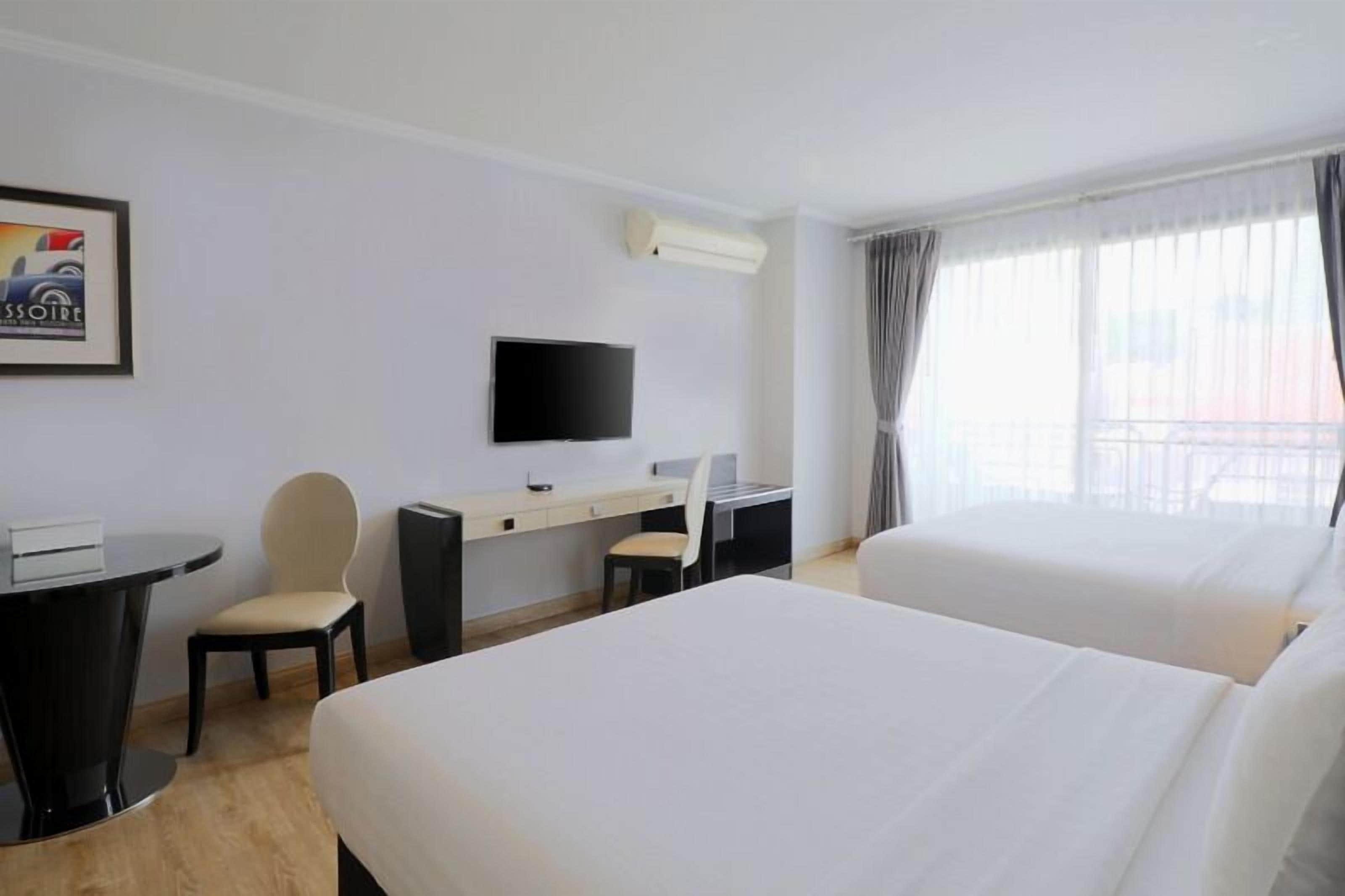 Une chambre d’hôtel avec deux lits, un bureau avec une chaise, une télévision et une fenêtre avec des rideaux.