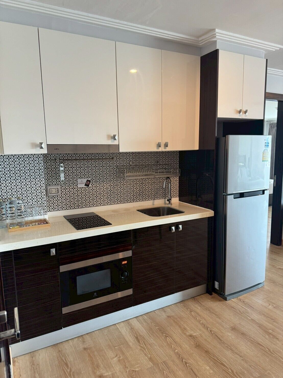 A modern kitchen with a built-in oven, a stainless steel refrigerator, and a patterned backsplash.