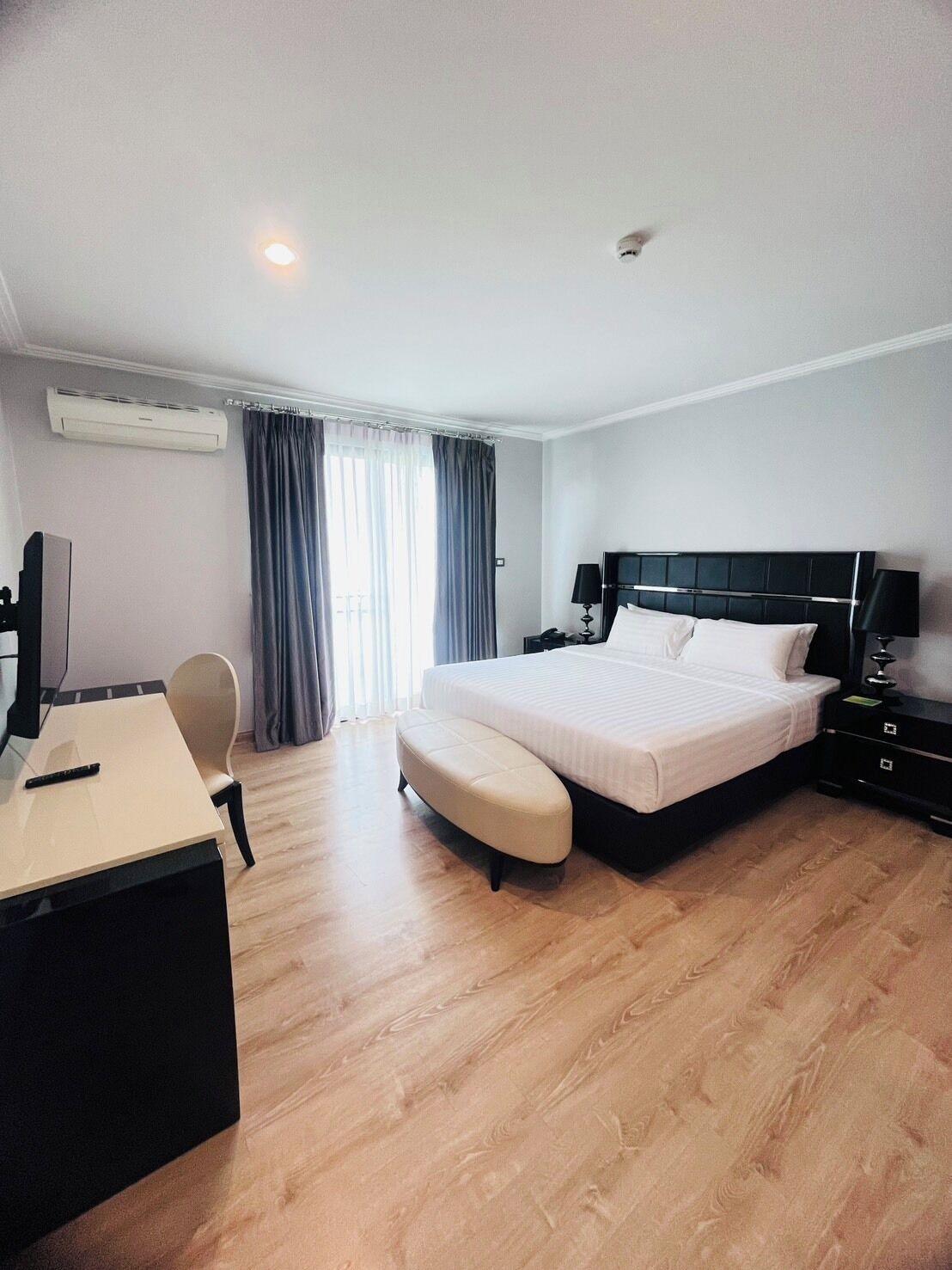 A hotel room with a bed, a desk, a chair, and an air conditioning unit.