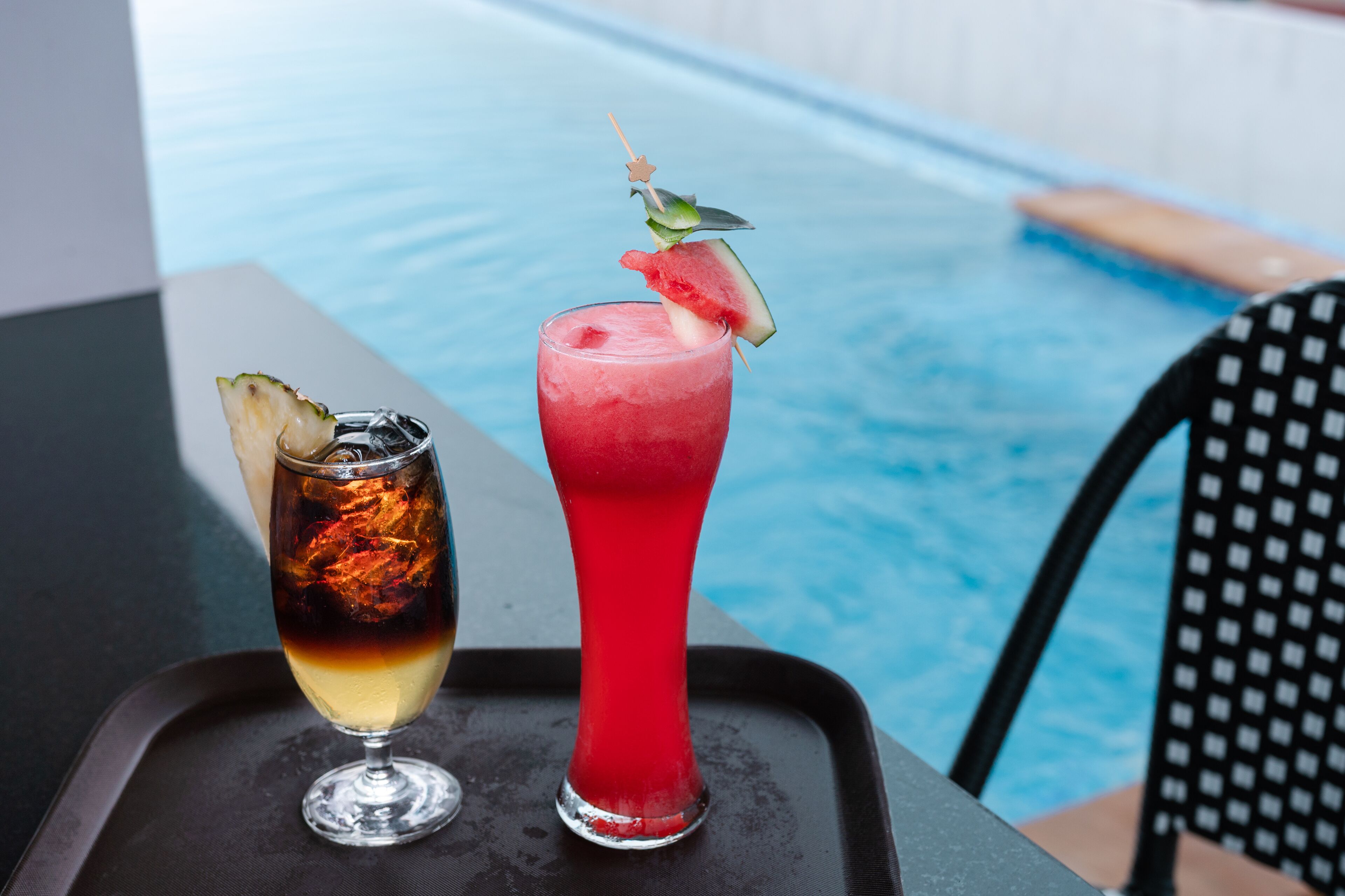 Two cocktails on a tray by a poolside.