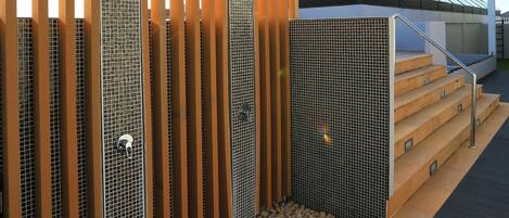 A modern outdoor shower area with a wooden pergola, metal mesh panels, and a glass roof.