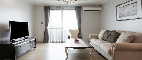 A modern living room with a flat-screen TV, a sofa, a coffee table, and a chandelier.