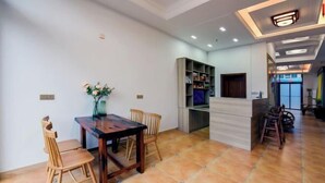 A dining area with a wooden table and chairs, a bookshelf, and a modern kitchen area. - Taicang Your Crown Trip Inn (Taicang)
