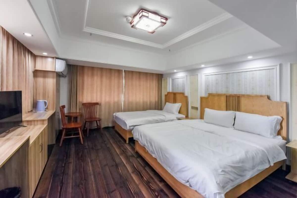 A hotel room with two beds, a desk with a chair, a TV, and a wooden floor.
