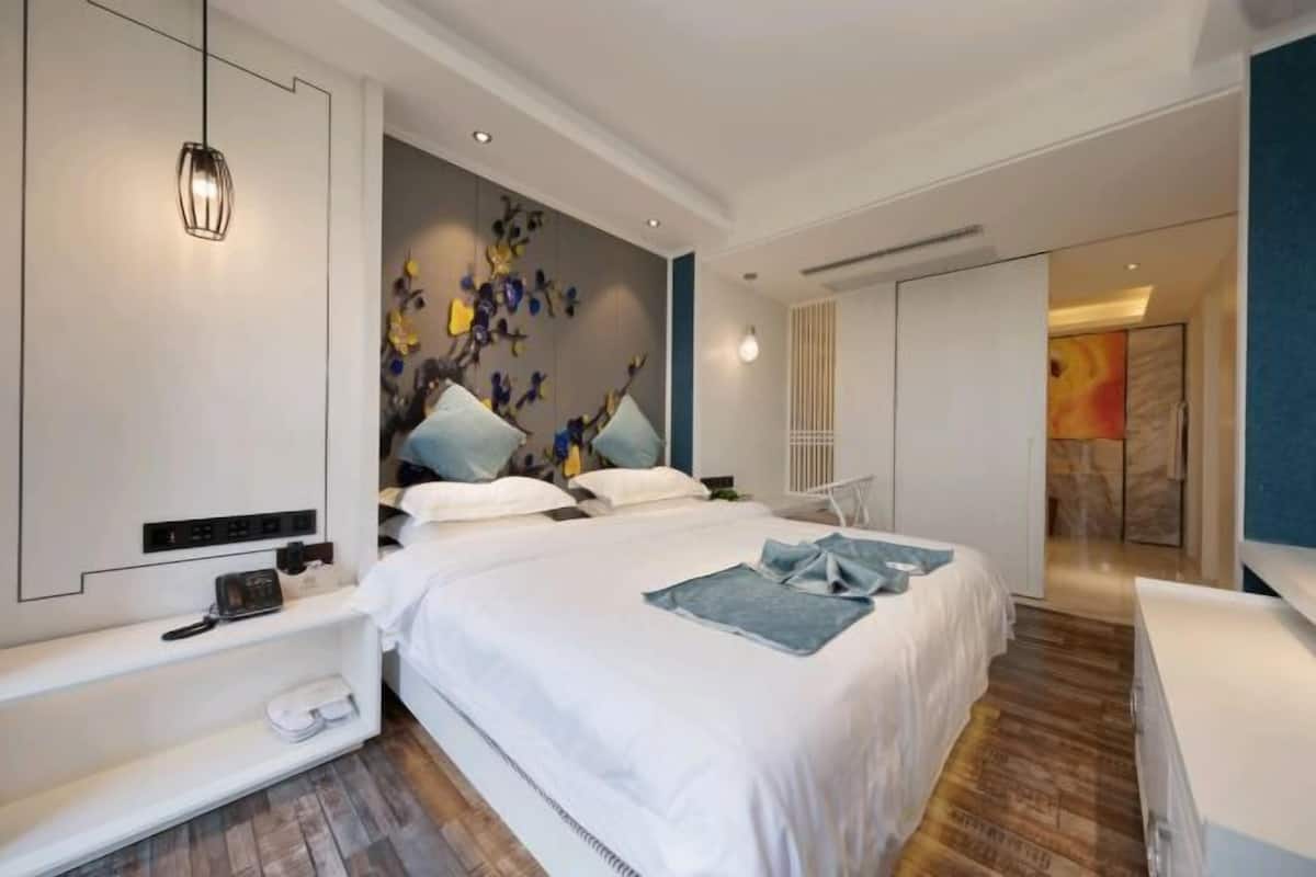 A modern bedroom with a large bed, bedside tables, a wall-mounted light fixture, and a decorative wall piece.