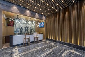 A reception area with a marble floor, a reception desk, two chairs, a wall-mounted TV, and a decorative light fixture. - Feilite Hotel (Kunming)