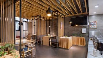 A restaurant with wooden beams, tables, chairs, and a brick wall.