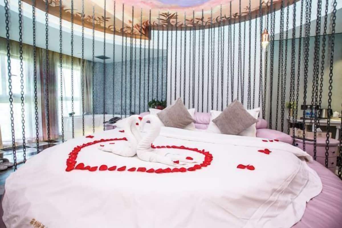 A bed with a heart-shaped arrangement of rose petals and a swan-shaped towel.