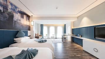 A modern hotel room with two beds, a TV, a desk, and a view of the cityscape.