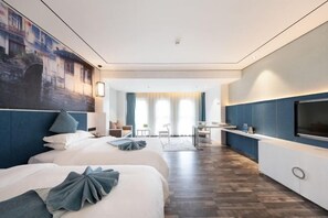 Quarto de hotel moderno com duas camas, televisão, escrivaninha e vista para a cidade.