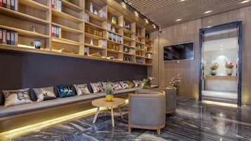 A modern lobby with a long sofa, wooden bookshelves, a round coffee table, and a marble floor.