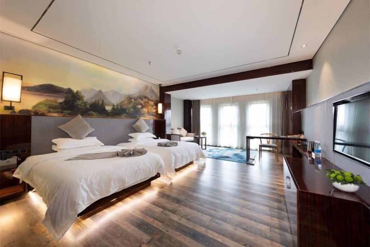 A hotel room with two beds, a dining area, a TV, and a painting on the wall.