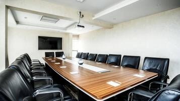 A conference room with a long wooden table, black leather chairs, a flat-screen TV, and a projector mounted on the ceiling.