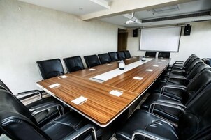 Un salón de conferencias con una larga mesa de madera, sillas de cuero negro y una pantalla para proyector.
