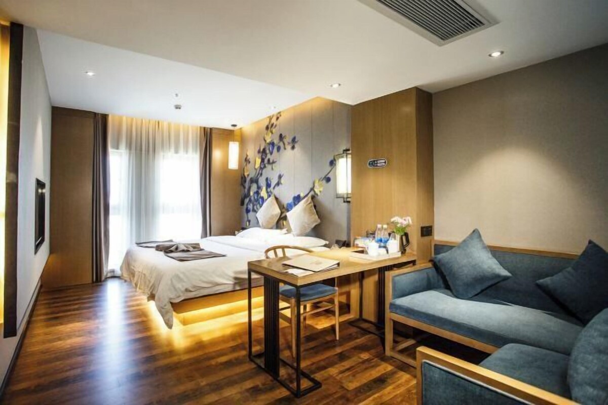 Quarto de hotel moderno com uma cama, uma mesa com cadeira, um sofá e uma parede decorativa com flores azuis.