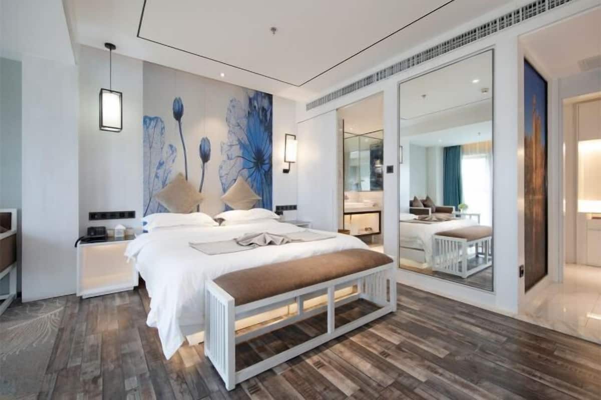 A modern hotel room with a large bed, a bench, a nightstand, a bedside table, and a mirror.
