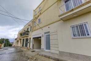 Residential building with a balcony and potted plants, featuring a garage door and metal bars on the windows.