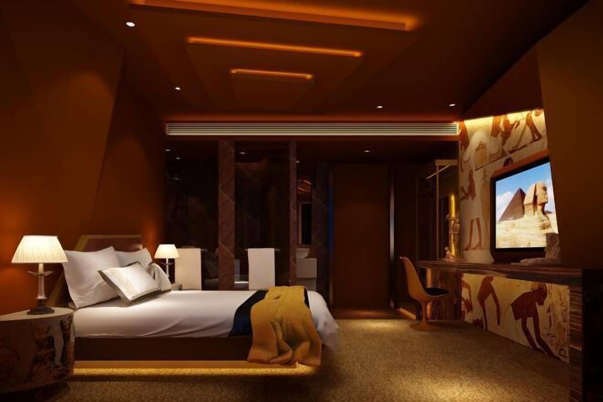 A modern hotel room with a large bed, a desk with a chair, a television, and wall art.