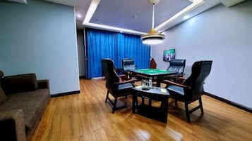 Una habitación con mesa de billar, cuatro sillas, un sofá y una lámpara en el techo.