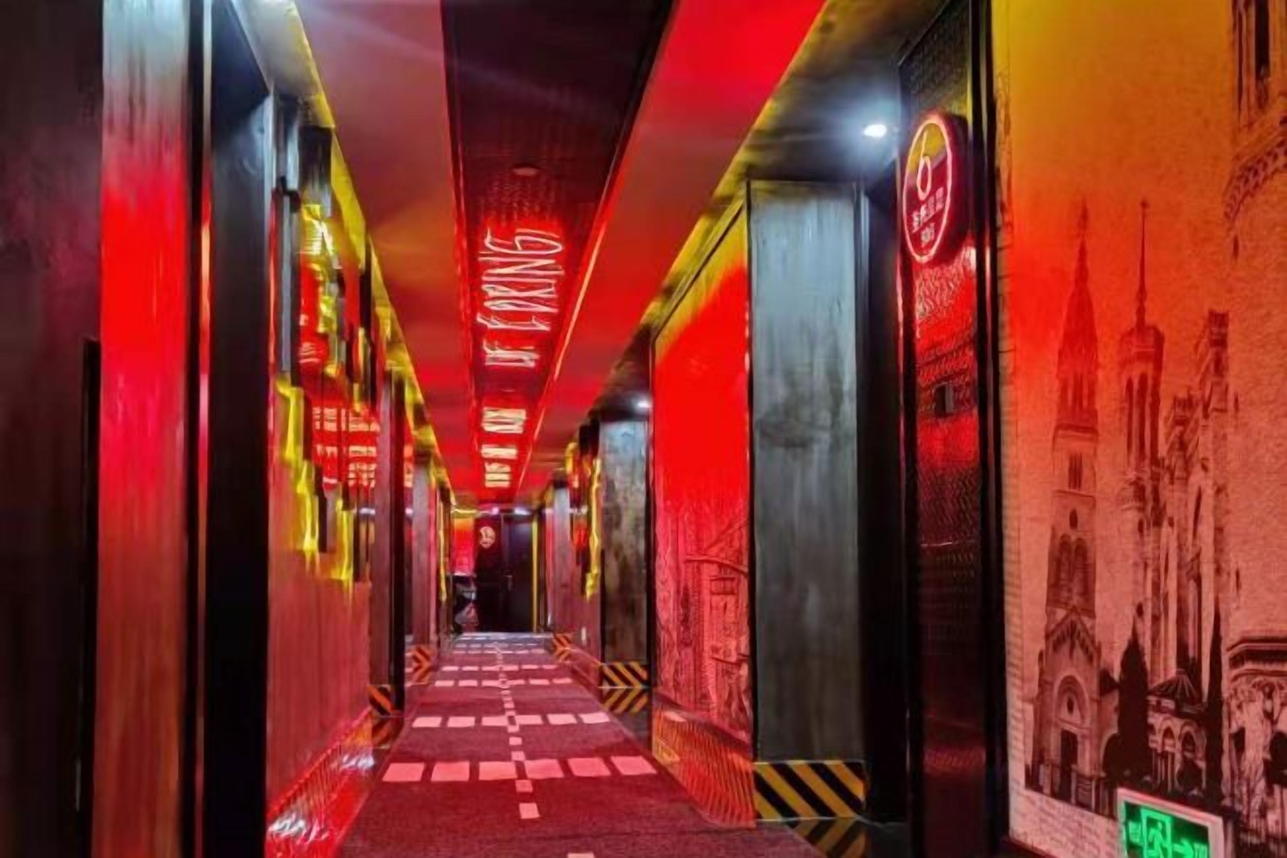 A corridor with a red carpet, neon signs, and a wall with a building illustration.