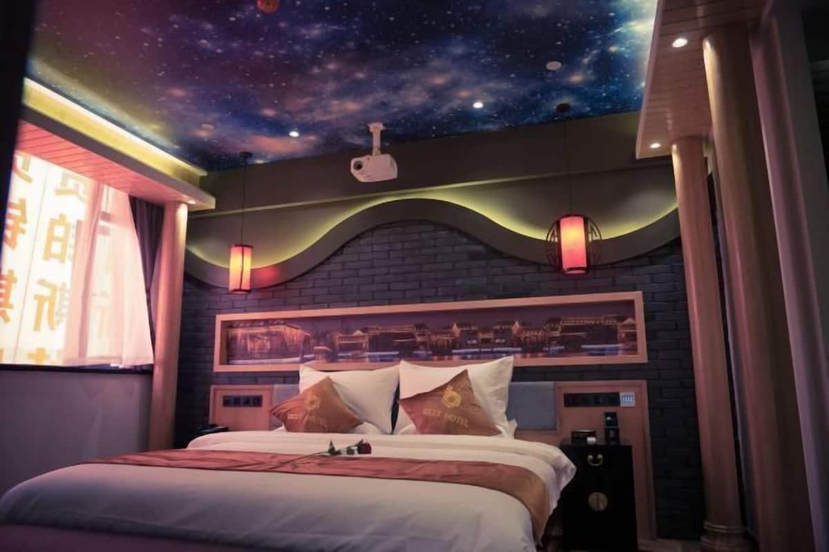 A hotel room with a starry night ceiling, a brick accent wall, and a bed with decorative pillows.