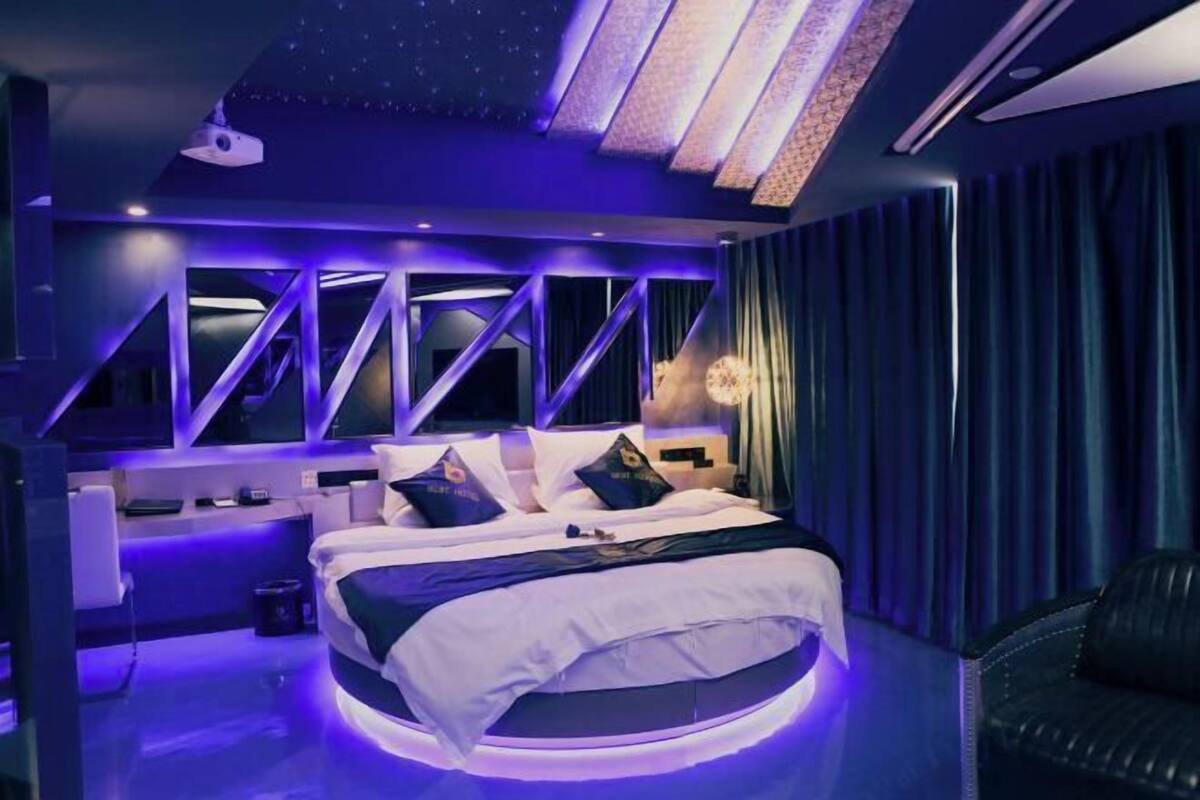 A modern bedroom with a bed centered in the room, a nightstand, and a large window with a view.