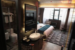 Habitación de hotel con cama, televisión, lavabo y ducha.