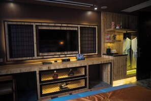 Una habitación moderna con un mueble de televisión de madera, estantes con objetos y una cama con una manta azul.