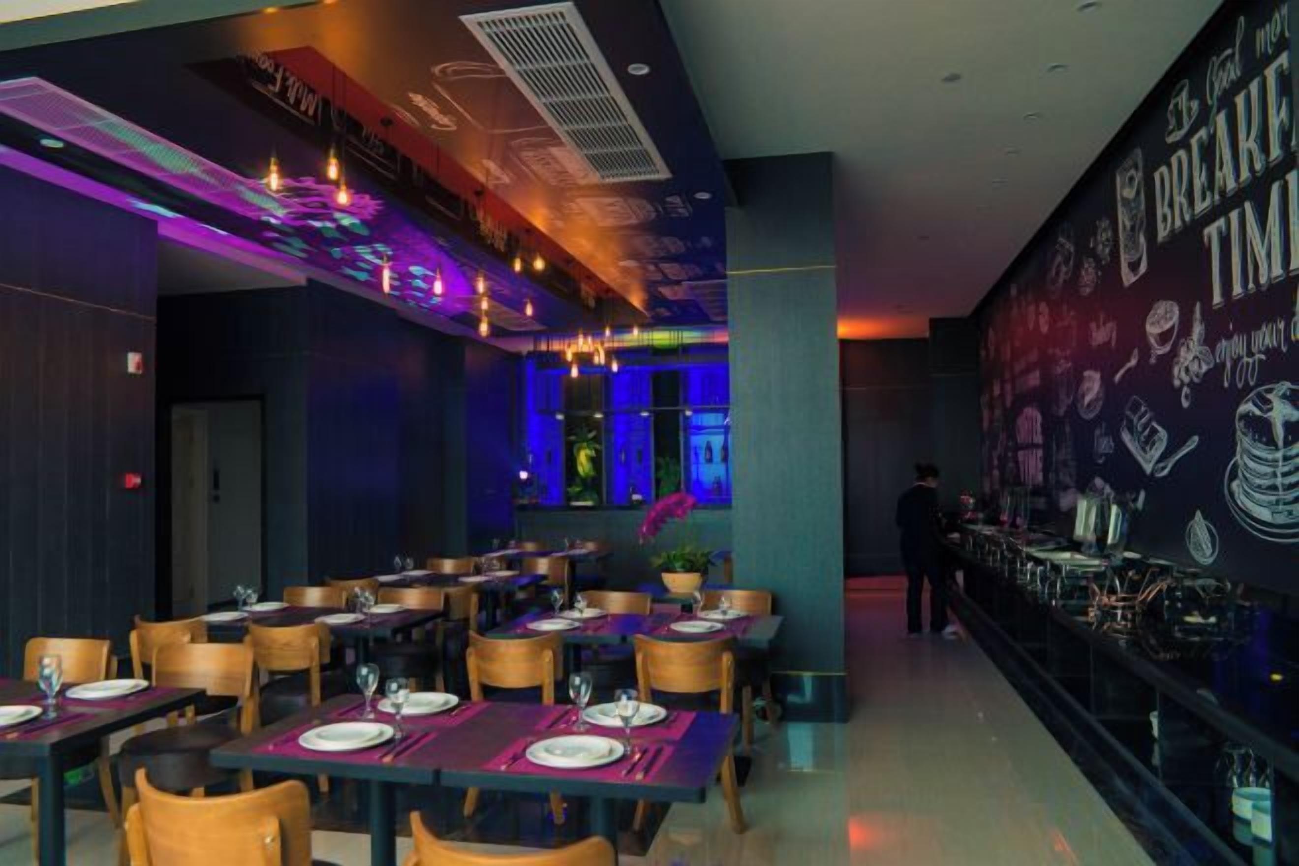 Un restaurante con mesas dispuestas para comer, una zona de bar y una pared con diversos gráficos relacionados con bebidas.