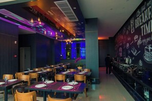 Un restaurante con mesas dispuestas para comer, una zona de bar y una pared con diversos gráficos relacionados con bebidas.