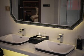 Un baño con dos lavamanos blancos, un espejo grande con un marco decorativo y un jabonera negra.