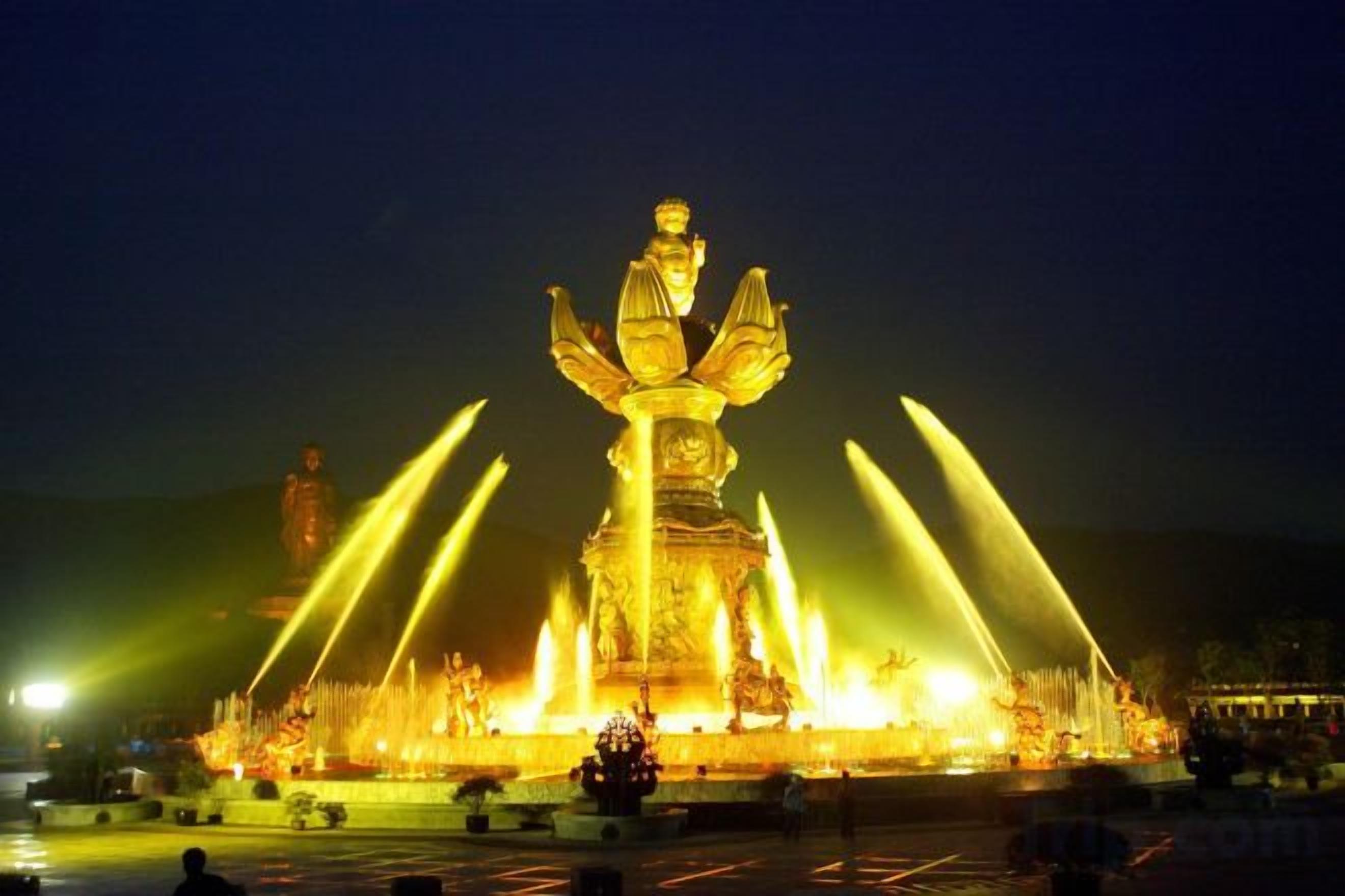 A large illuminated statue with water jets at night.