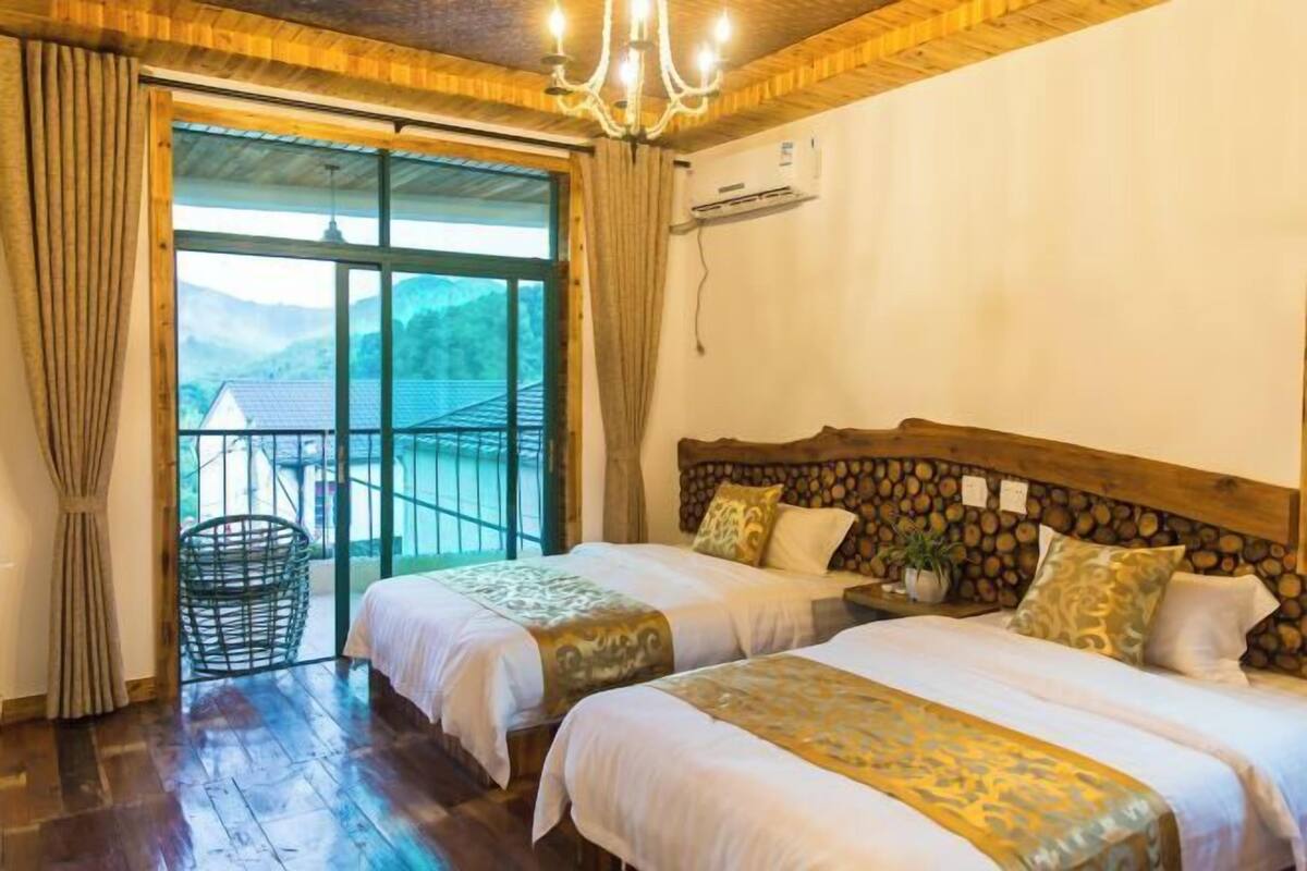 A room with two beds, a large window, a chandelier, and a view of the outdoors.