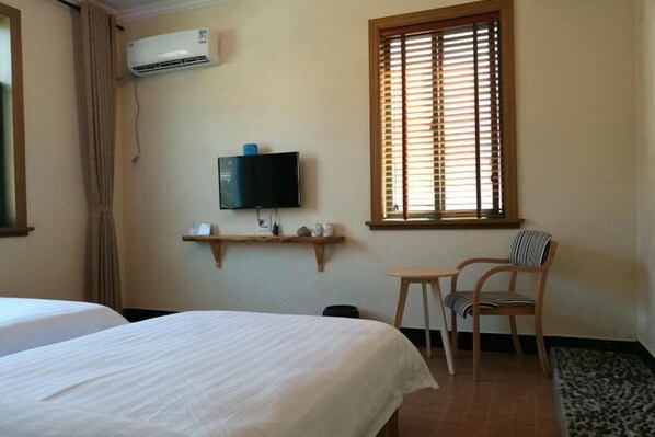 A hotel room with two beds, a TV mounted on the wall, a window with blinds, a small table, and a chair. - Qingmei Zhuma Inn (Deqing)