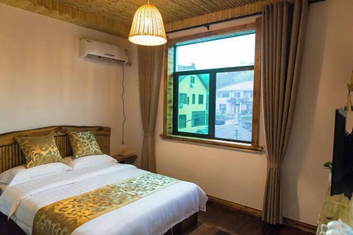 A bedroom with a wooden headboard, a bed with patterned bedding, a window with curtains, and an air conditioning unit on the wall.