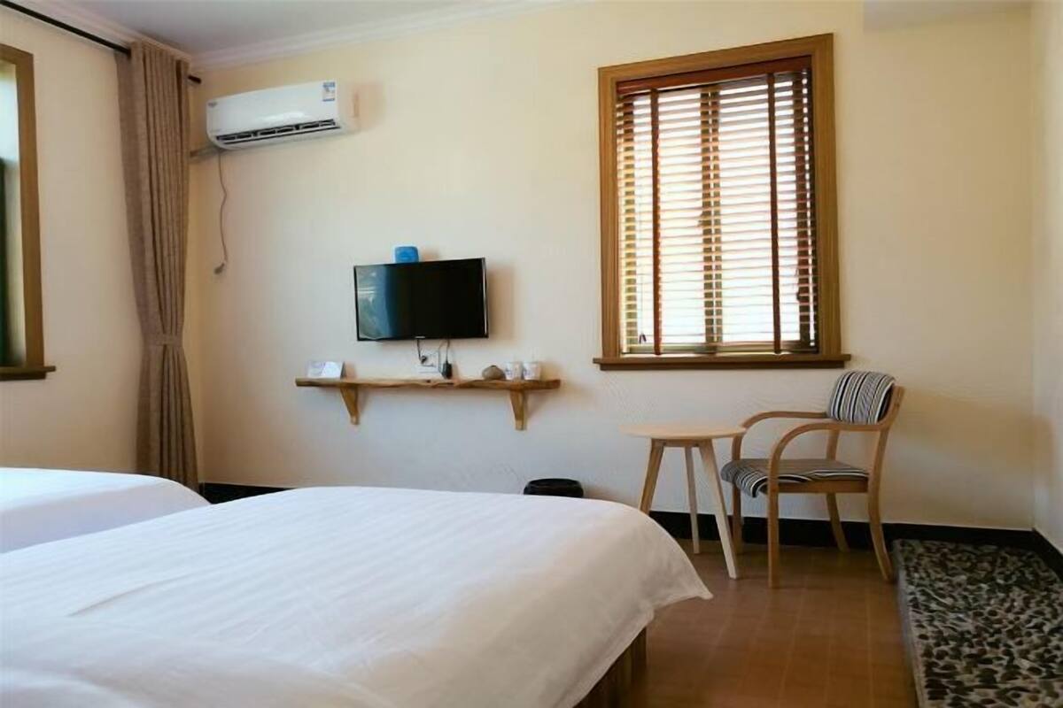 A hotel room with a bed, a television, a window with blinds, a chair, and a small table.