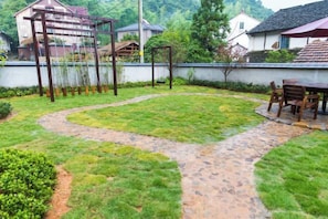 A garden with a stone pathway, a wooden pergola, and a table with chairs. - Qingmei Zhuma Inn (Deqing)