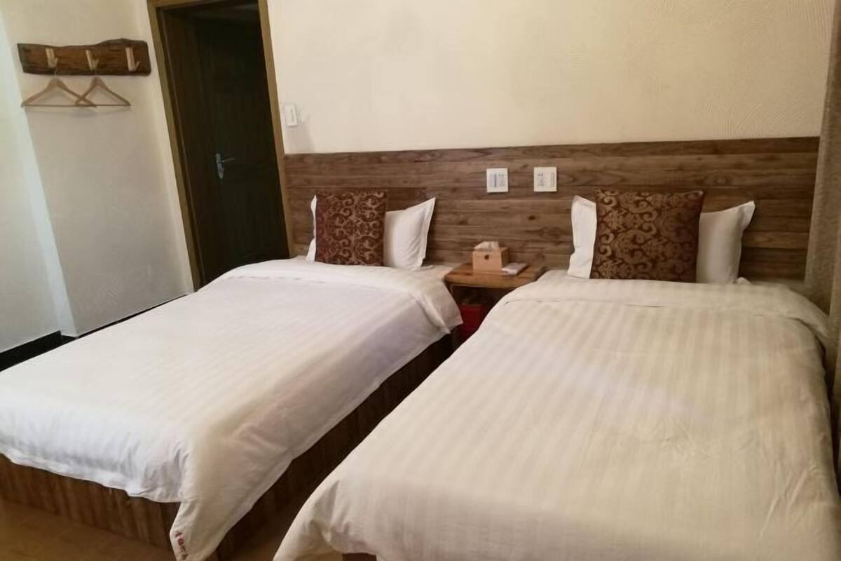 Two single beds with wooden headboards, a small bedside table, and a hanging coat rack.