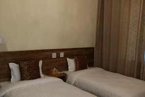 A hotel room with two beds, wooden headboard, and a nightstand with a lamp. - Qingmei Zhuma Inn (Deqing)