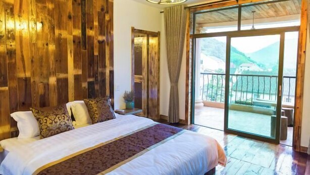 A bedroom with a large bed, wooden walls, and a balcony with a mountain view. - Qingmei Zhuma Inn (Deqing)