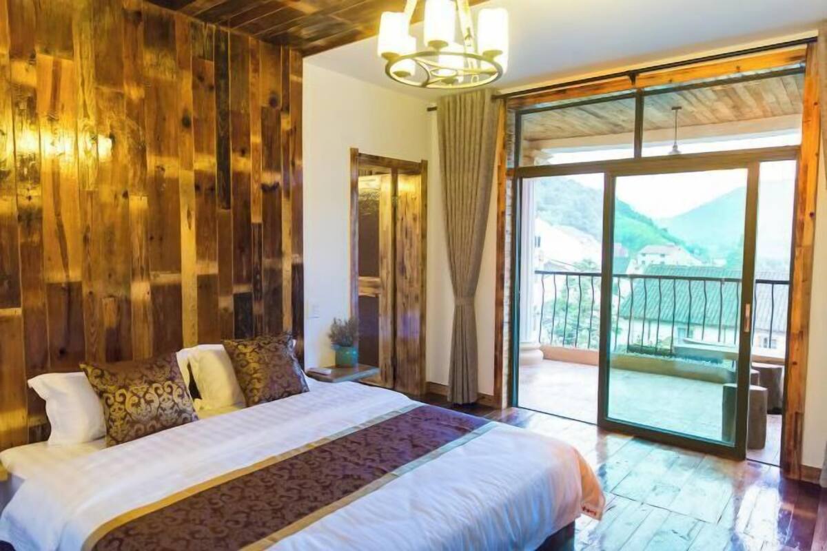A bedroom with a large bed, wooden walls, and a balcony with a mountain view.