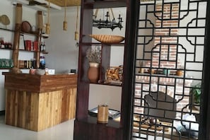 A wooden reception desk with shelves of decorative items, a brick wall, and a decorative screen. - Qingmei Zhuma Inn (Deqing)