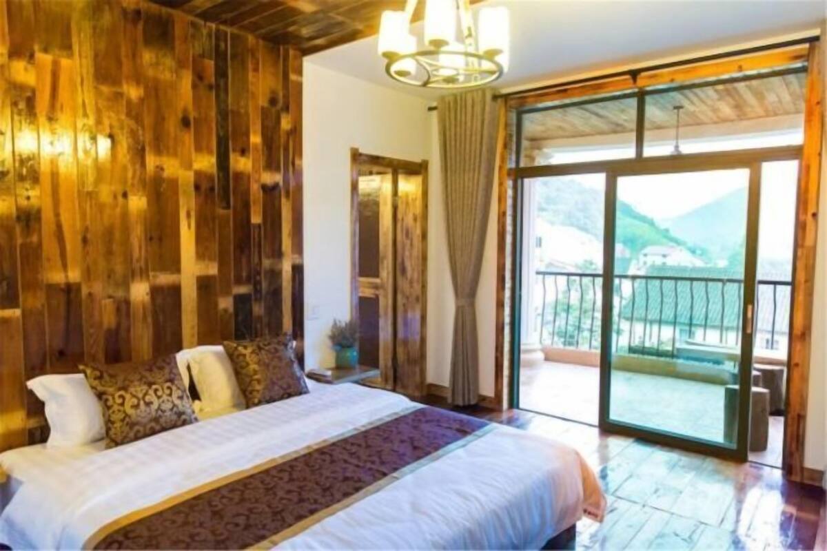 A bedroom with a large bed, wooden walls, a chandelier, and a balcony with a view.