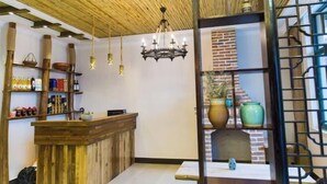 A reception area with a wooden counter, shelves with bottles and books, a chandelier, and a brick fireplace. - Qingmei Zhuma Inn (Deqing)