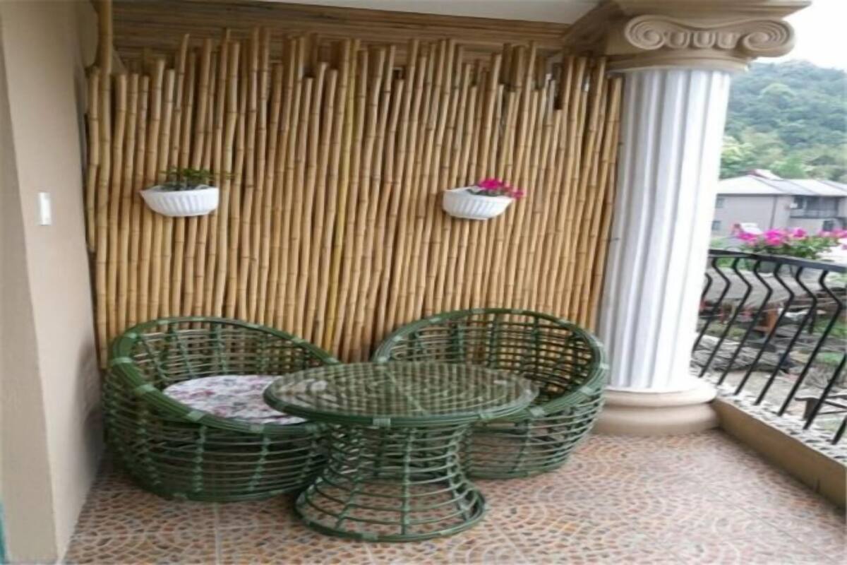 A balcony with wicker furniture, a bamboo wall, and two potted plants.