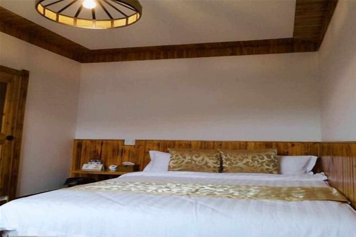 A bedroom with a wooden headboard, a bed with white bedding, a bedside table with a lamp, and a hanging light fixture.