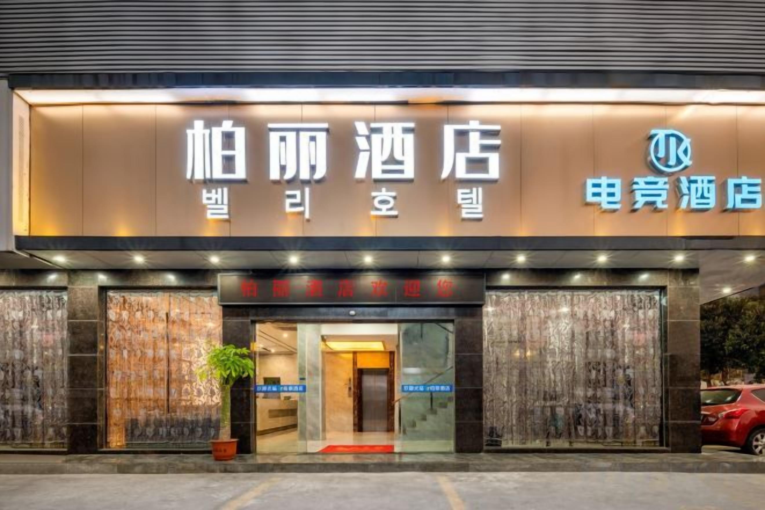 A hotel entrance with a modern facade, illuminated signage, and a visible entrance door.
