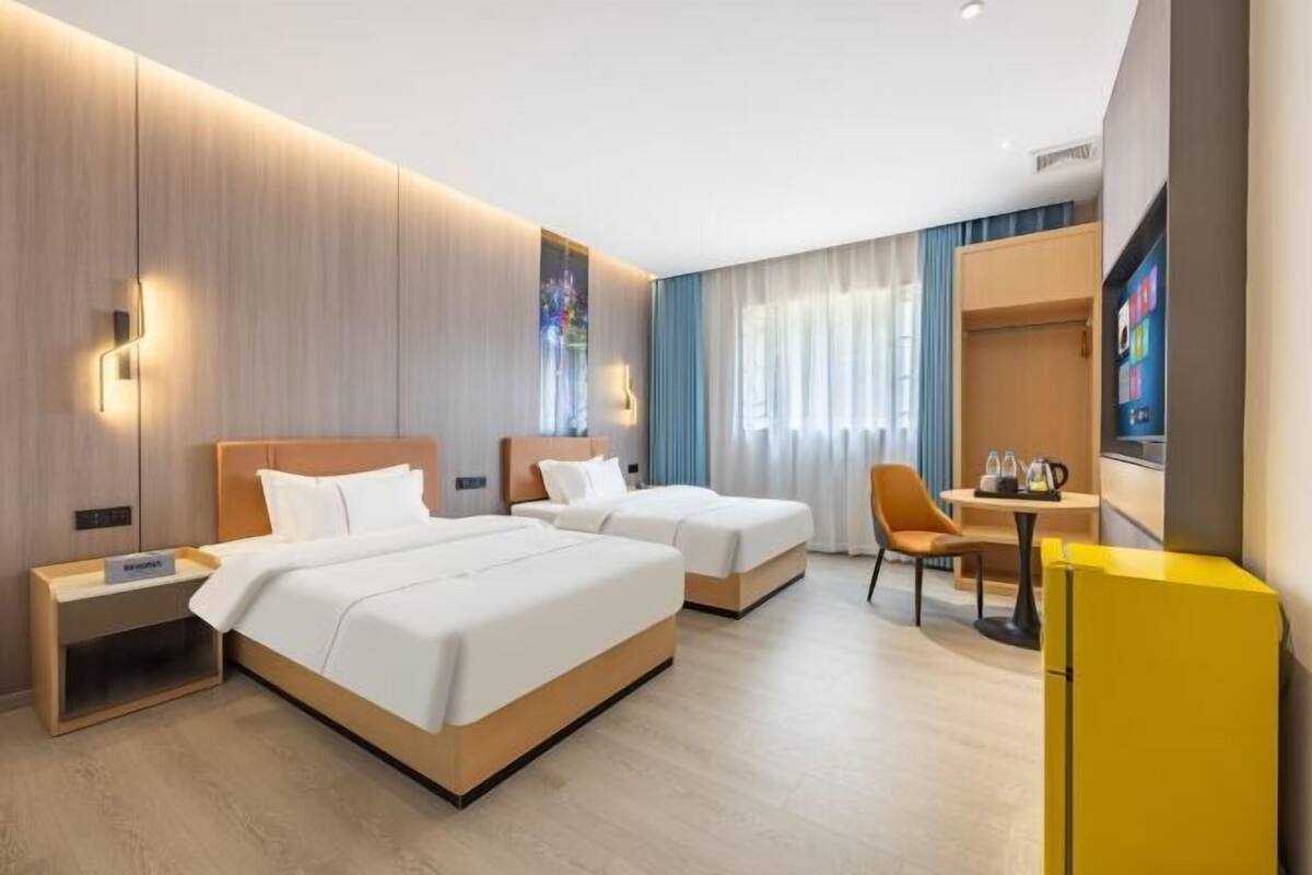 A hotel room with two beds, a desk, a chair, a television, and a minibar.