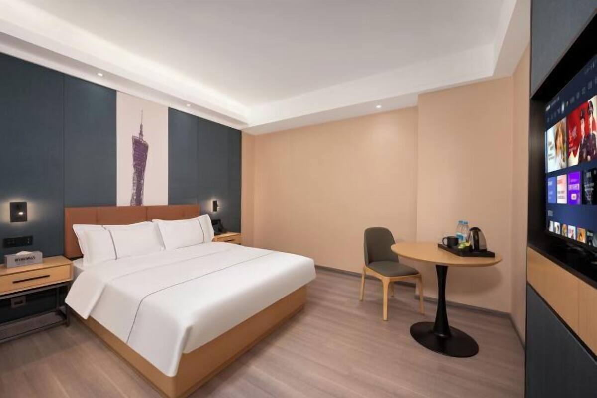 A modern hotel room with a large bed, a small desk, a chair, and a TV on the wall.