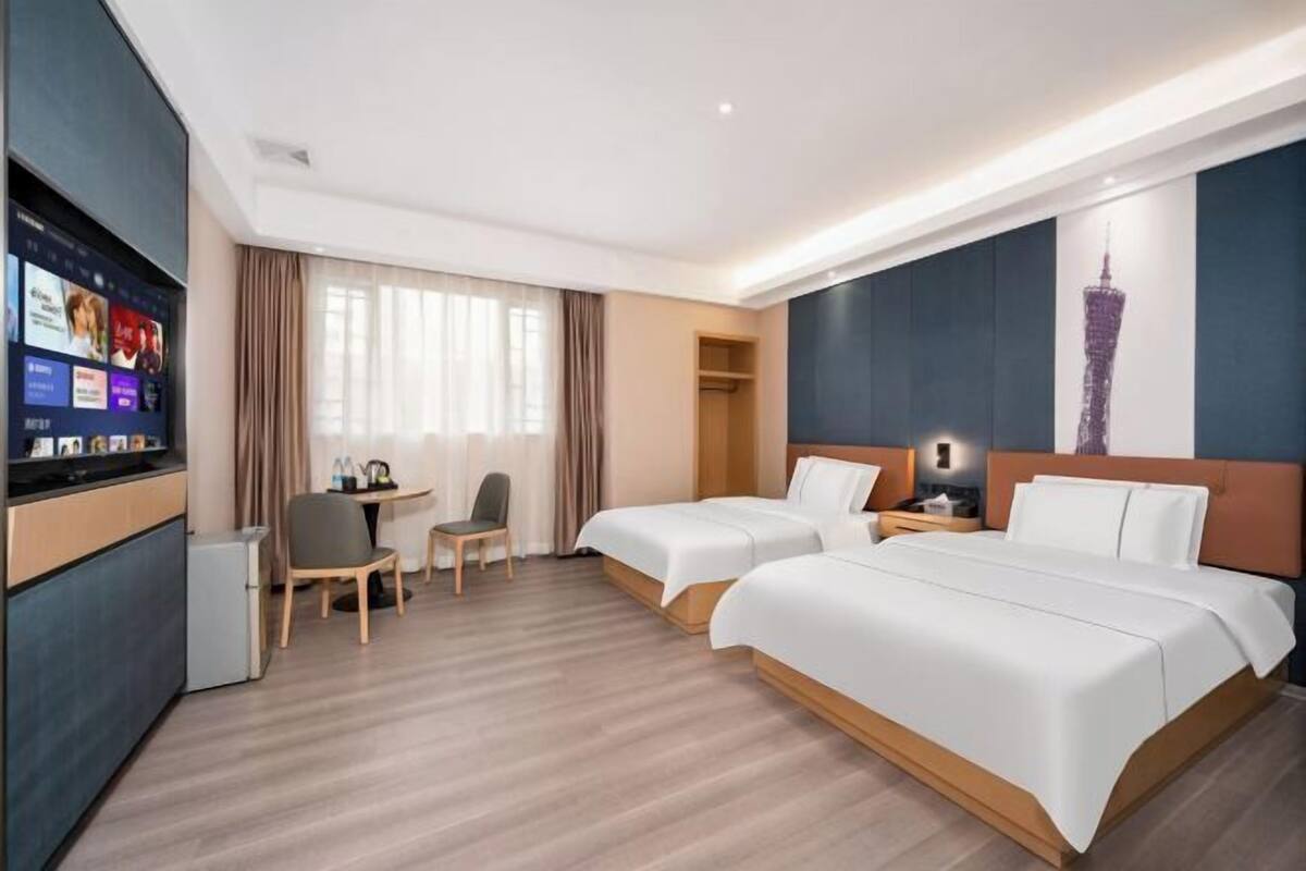 A hotel room with two beds, a desk, a chair, a TV, and a wardrobe.